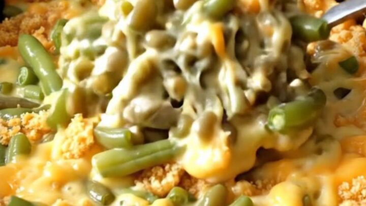 A close-up view of the creamy green bean bake inside a black slow cooker insert, showing melted cheese and green beans.