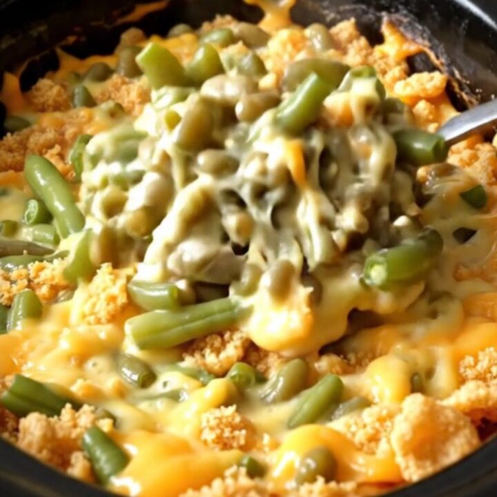 A close-up view of the creamy green bean bake inside a black slow cooker insert, showing melted cheese and green beans.