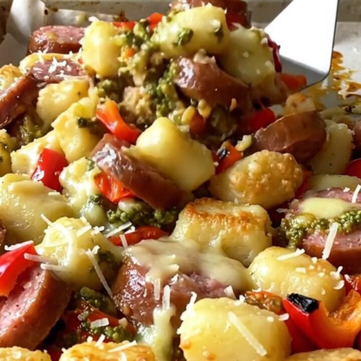 A sheet pan filled with golden-brown gnocchi, sliced smoked sausage, and roasted red bell peppers coated in pesto.