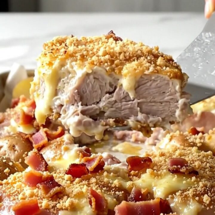 A sheet pan filled with golden-brown pork medallions and roasted baby potatoes topped with creamy sauce and bacon.
