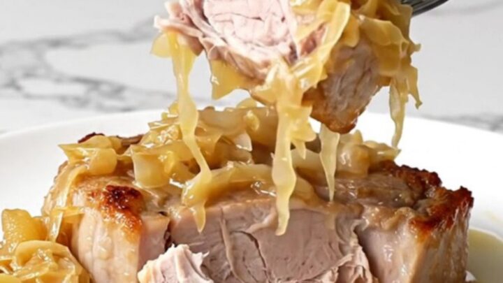 A close-up of tender, slow-cooked pork steaks topped with sauerkraut and sliced apples on a white plate.