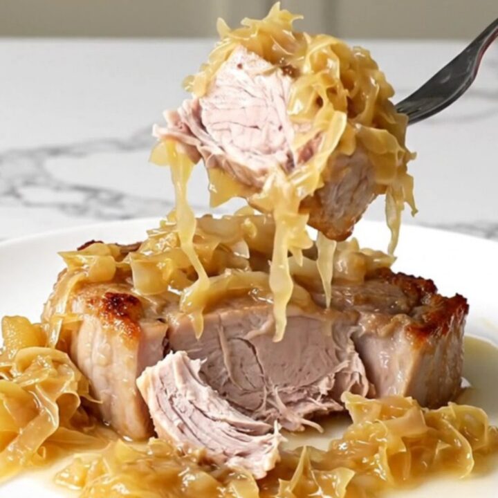 A close-up of tender, slow-cooked pork steaks topped with sauerkraut and sliced apples on a white plate.