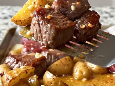 A sheet pan filled with golden roasted potato chunks and deep brown, tender sirloin steak bites topped with fresh parsley.