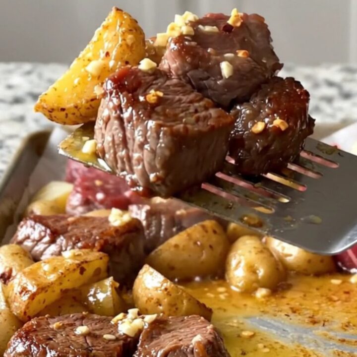 A sheet pan filled with golden roasted potato chunks and deep brown, tender sirloin steak bites topped with fresh parsley.