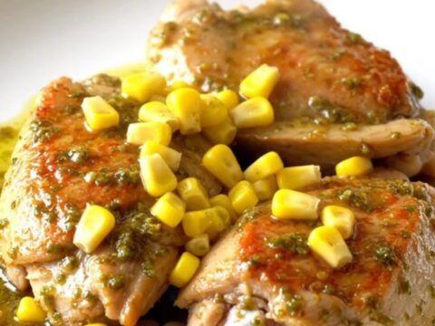 A close-up of tender chili lime chicken thighs served with sweet corn on a white plate.