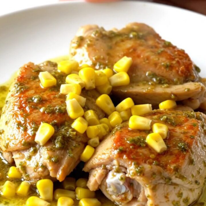 A close-up of tender chili lime chicken thighs served with sweet corn on a white plate.