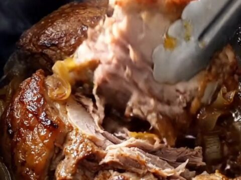 A rustic slow-cooked pork shoulder served on a white platter with onions and garlic.