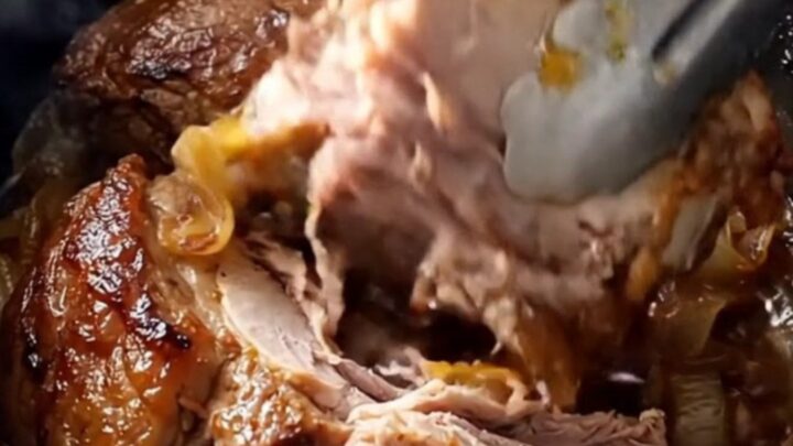 A rustic slow-cooked pork shoulder served on a white platter with onions and garlic.