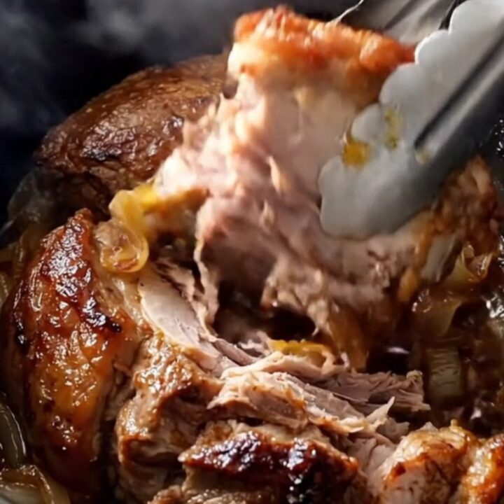 A rustic slow-cooked pork shoulder served on a white platter with onions and garlic.
