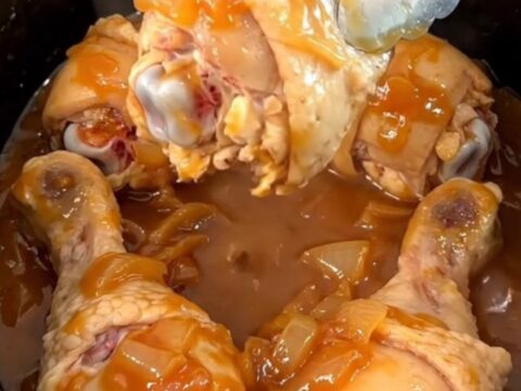 A close-up of slow-cooked chicken drumsticks in a rich, dark brown sugar and tomato chili sauce.