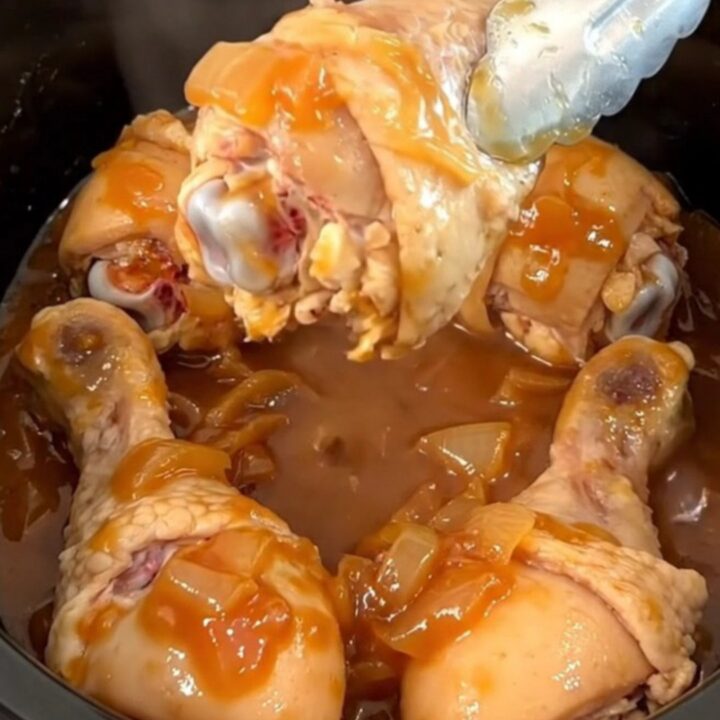 A close-up of slow-cooked chicken drumsticks in a rich, dark brown sugar and tomato chili sauce.