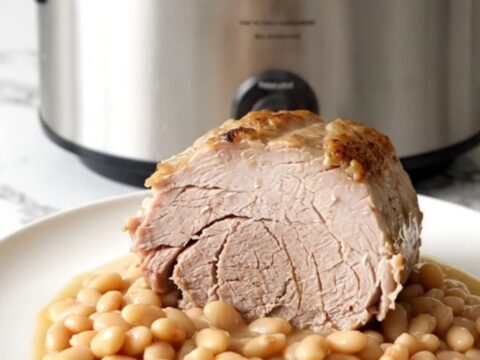 A slow-cooked boneless pork loin roast served with white beans on a white plate.