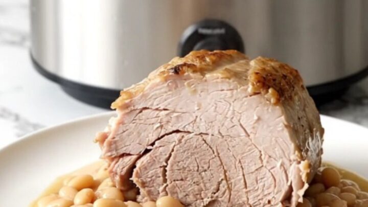 A slow-cooked boneless pork loin roast served with white beans on a white plate.