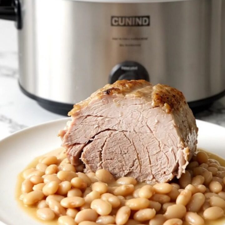 A slow-cooked boneless pork loin roast served with white beans on a white plate.
