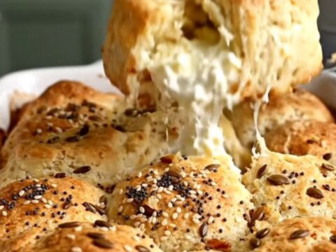 A top-down view of a golden-brown everything bagel pull-apart biscuit bake in a white ceramic dish.