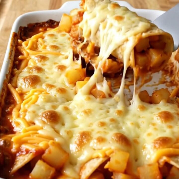 A top-down view of a rectangular baking dish filled with corn tortilla rolls covered in red sauce and melted cheddar cheese.