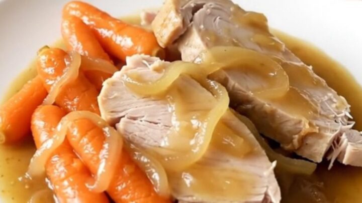 A slow cooker filled with tender turkey breast slices and baby carrots in a rich, savory onion gravy.