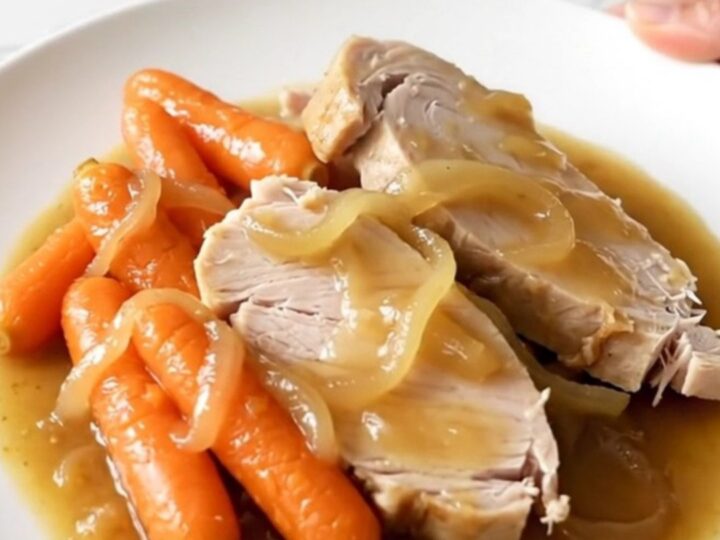 A slow cooker filled with tender turkey breast slices and baby carrots in a rich, savory onion gravy.