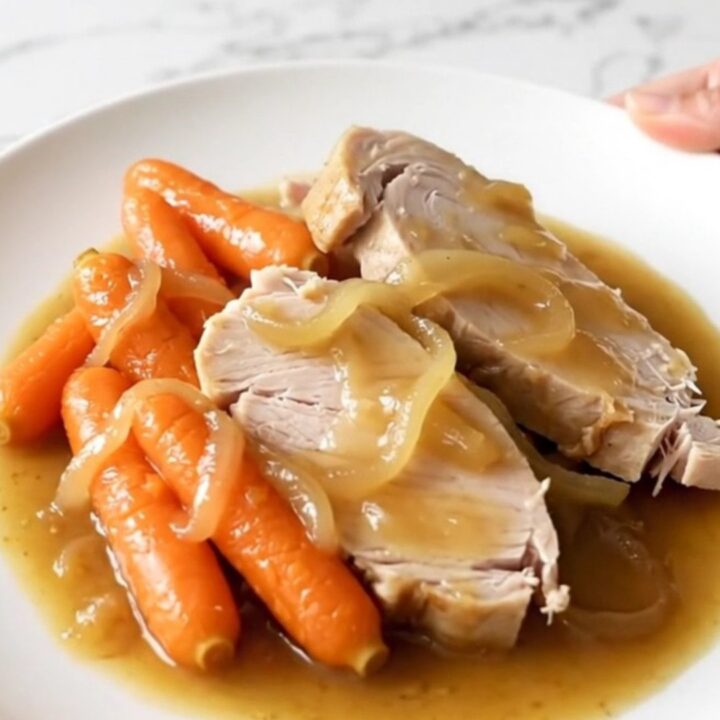 A slow cooker filled with tender turkey breast slices and baby carrots in a rich, savory onion gravy.