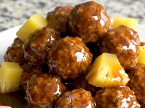 A close-up of tender turkey meatballs covered in a glossy dark brown Huli Huli sauce with chunks of pineapple.