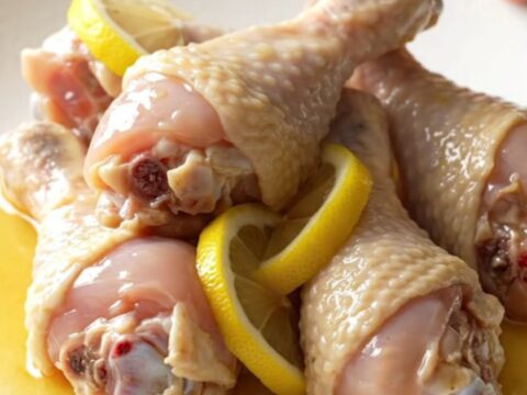 A close-up of tender, braised chicken drumsticks in a glossy lemonade and soy sauce glaze, topped with soft lemon slices.