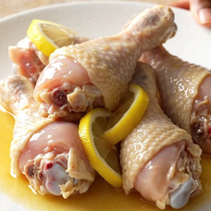 A close-up of tender, braised chicken drumsticks in a glossy lemonade and soy sauce glaze, topped with soft lemon slices.