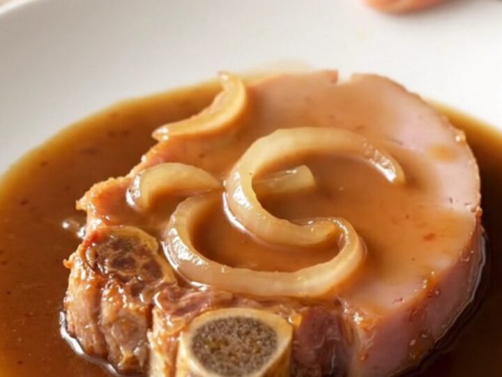 A close-up of a tender bone-in ham steak glazed in a dark, rich coffee gravy with soft onions on a white plate.