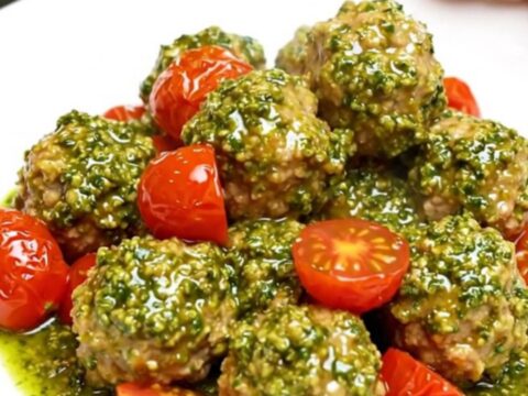 A white plate filled with chicken meatballs and cherry tomatoes covered in vibrant green pesto sauce.