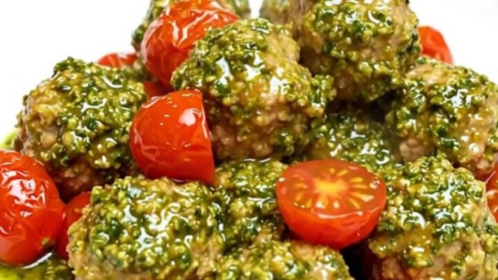 A white plate filled with chicken meatballs and cherry tomatoes covered in vibrant green pesto sauce.