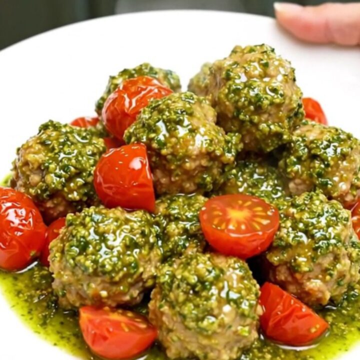 A white plate filled with chicken meatballs and cherry tomatoes covered in vibrant green pesto sauce.