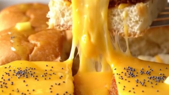 A close-up of golden-brown sliders in a baking dish with melted cheese and poppy seeds.