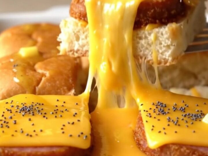 A close-up of golden-brown sliders in a baking dish with melted cheese and poppy seeds.