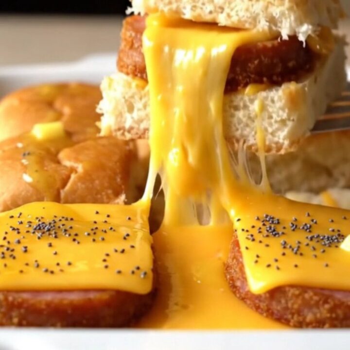A close-up of golden-brown sliders in a baking dish with melted cheese and poppy seeds.