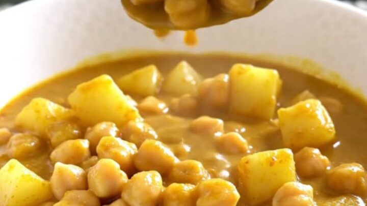 A close-up of a bowl filled with creamy coconut curry chickpea stew with visible potato cubes and chickpeas.