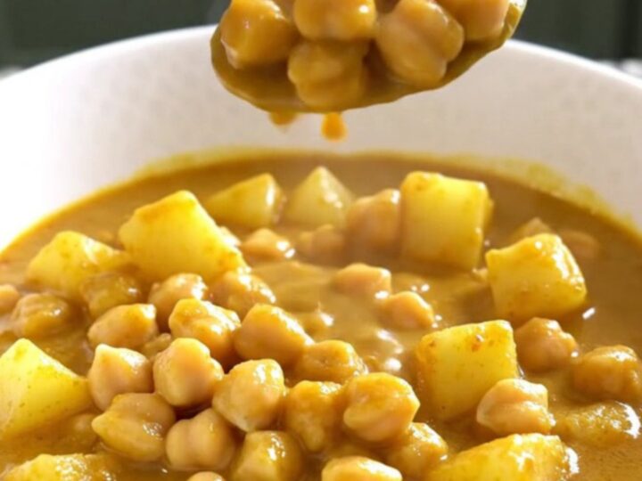 A close-up of a bowl filled with creamy coconut curry chickpea stew with visible potato cubes and chickpeas.