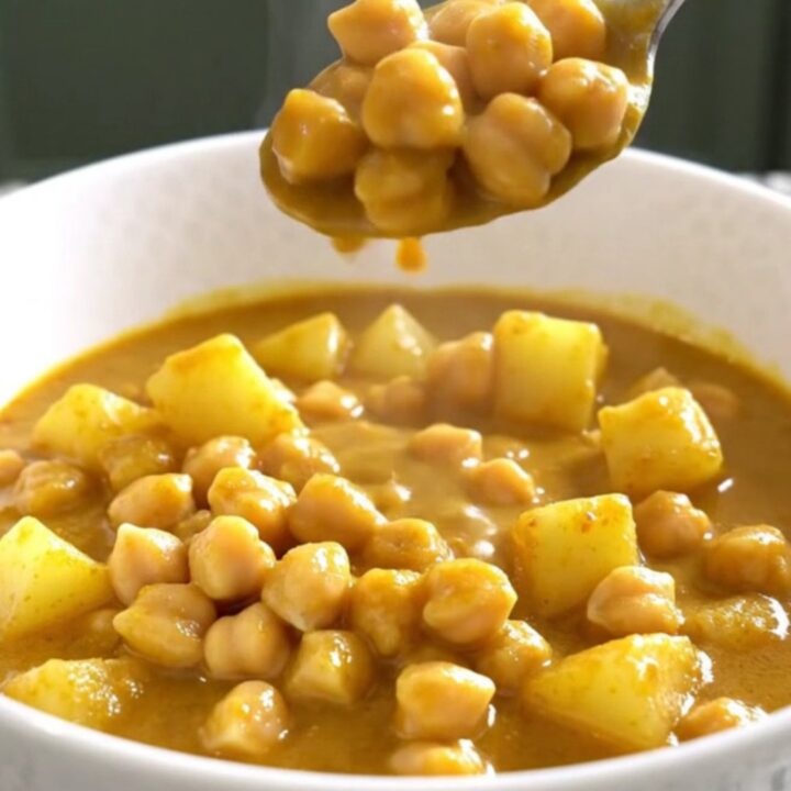 A close-up of a bowl filled with creamy coconut curry chickpea stew with visible potato cubes and chickpeas.