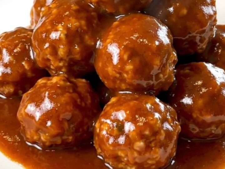 A slow cooker filled with turkey meatballs coated in a glossy, dark red maple sriracha sauce.