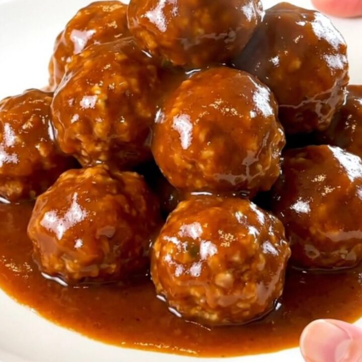 A slow cooker filled with turkey meatballs coated in a glossy, dark red maple sriracha sauce.