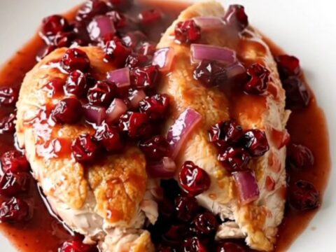 Crockpot cranberry chipotle chicken breasts served on a white plate with a thick, glossy red sauce.