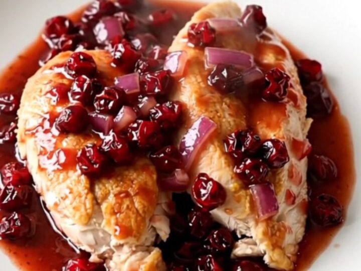 Crockpot cranberry chipotle chicken breasts served on a white plate with a thick, glossy red sauce.