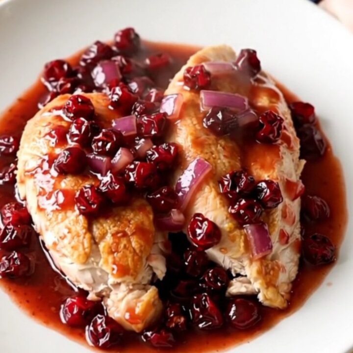 Crockpot cranberry chipotle chicken breasts served on a white plate with a thick, glossy red sauce.