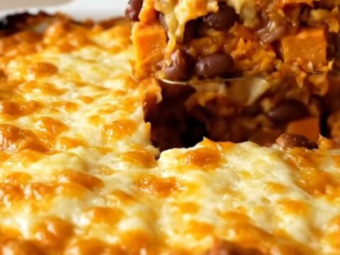 A top-down view of a rectangular baking dish filled with colorful sweet potato cubes, black beans, and red sauce.