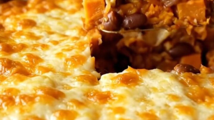 A top-down view of a rectangular baking dish filled with colorful sweet potato cubes, black beans, and red sauce.
