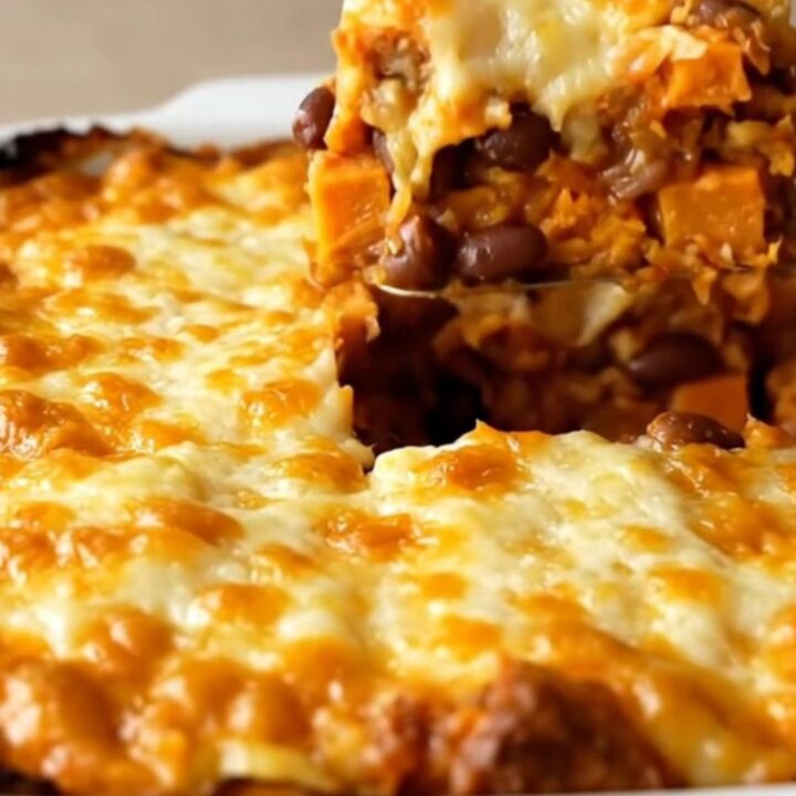 A top-down view of a rectangular baking dish filled with colorful sweet potato cubes, black beans, and red sauce.