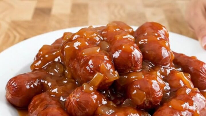 A slow cooker filled with mini sausages coated in a glossy, thick apricot chili sauce.