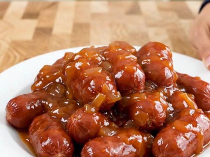 A slow cooker filled with mini sausages coated in a glossy, thick apricot chili sauce.