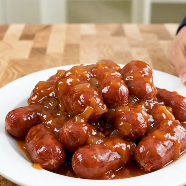 A slow cooker filled with mini sausages coated in a glossy, thick apricot chili sauce.
