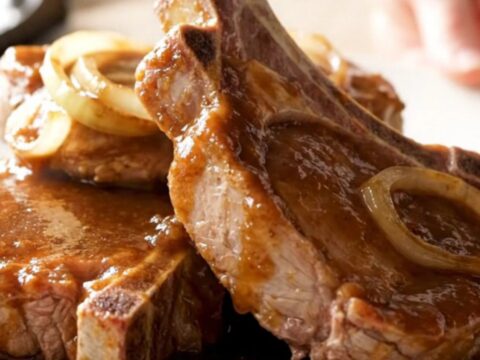 Four bone-in pork chops fanned out in a slow cooker, topped with sliced onions and steak sauce.