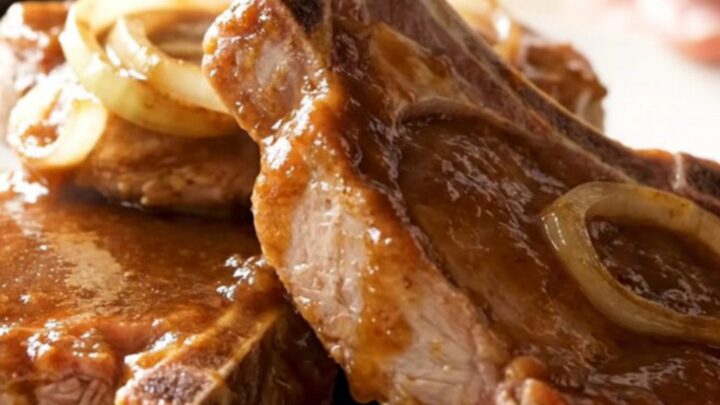 Four bone-in pork chops fanned out in a slow cooker, topped with sliced onions and steak sauce.
