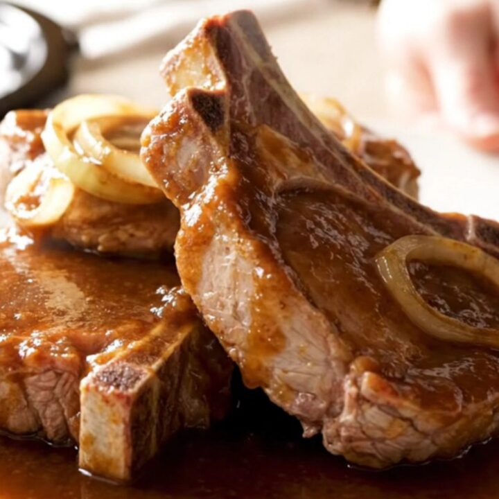 Four bone-in pork chops fanned out in a slow cooker, topped with sliced onions and steak sauce.